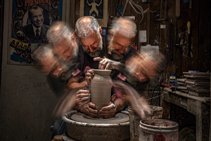 An abstract photograph of a man spinning clay. 