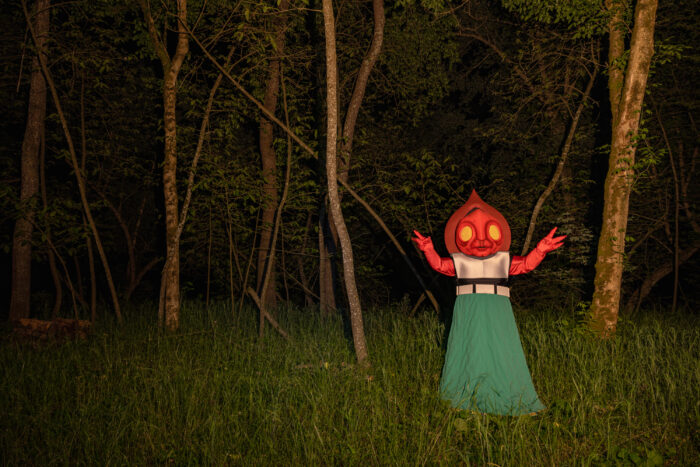 A photograph of the Flatwoods monster, a red cryptid, standing in the woods at night. 