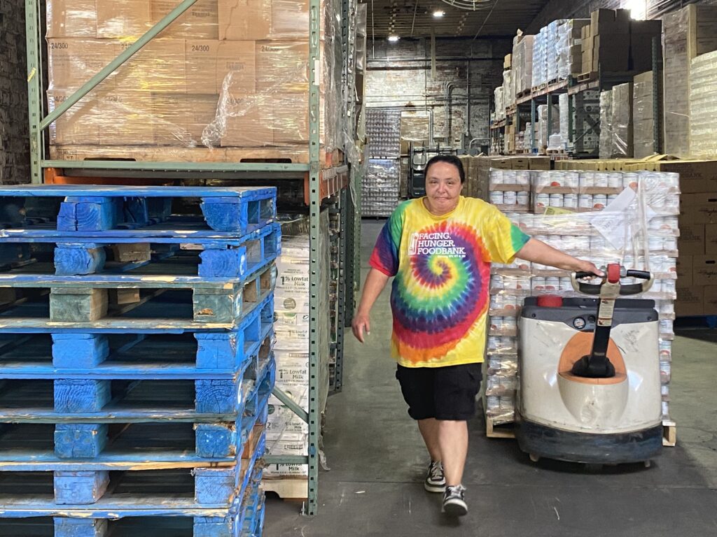 Lady in tie dyed t-shirt transporting large pallet in a warehouse.
