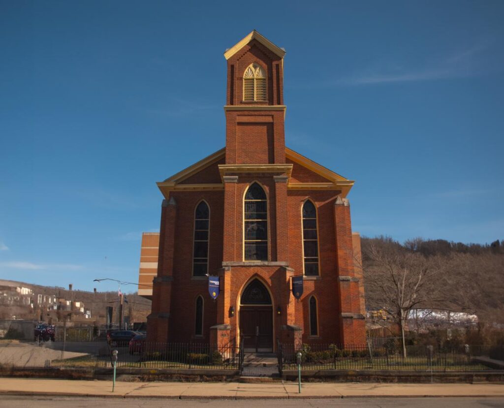 A brick building with a tall steeple stands against a blue sky.