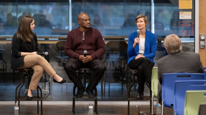 Two women and a man sitting on a stage addressing an audience
