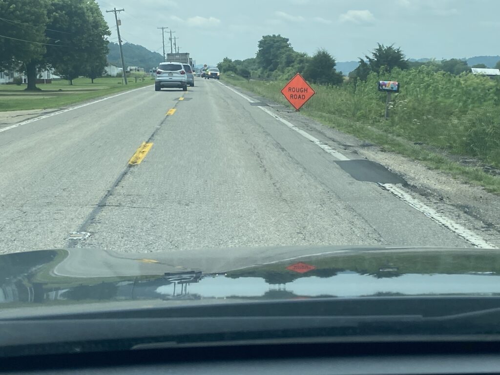 Two lane road with rough road sign and patching.