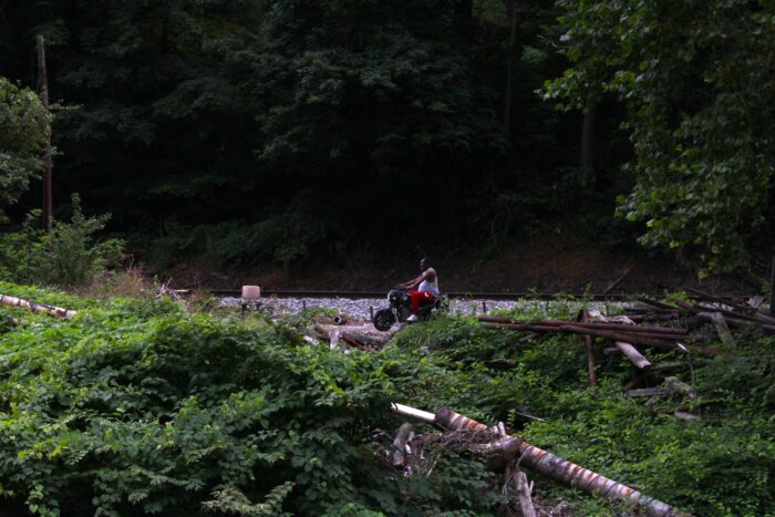 A man rides a scooter between the river and train tracks.