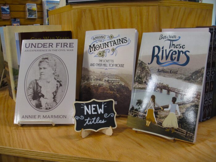 Three books sit on a wooden sale shelf next to a chalk sign that reads "New Books."