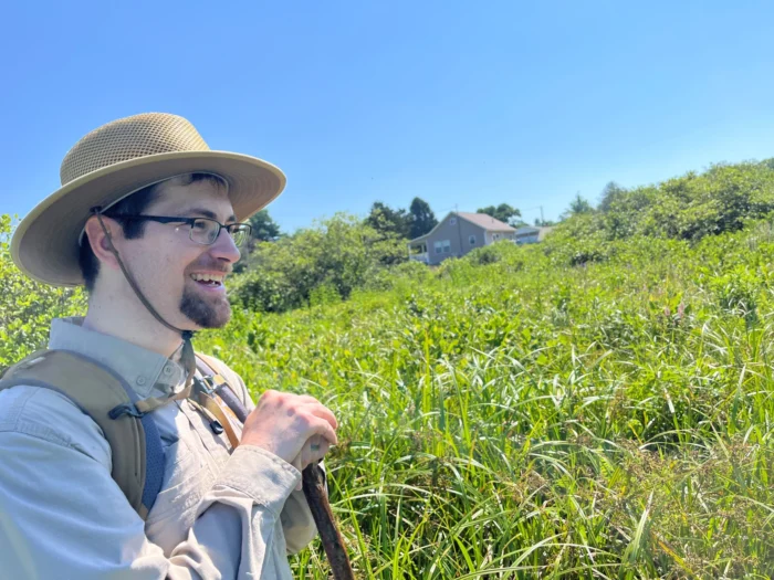 A white man standing in a field wearing a sun hat.