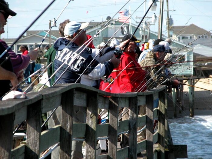 Several people stand on the side of a pier, outside.