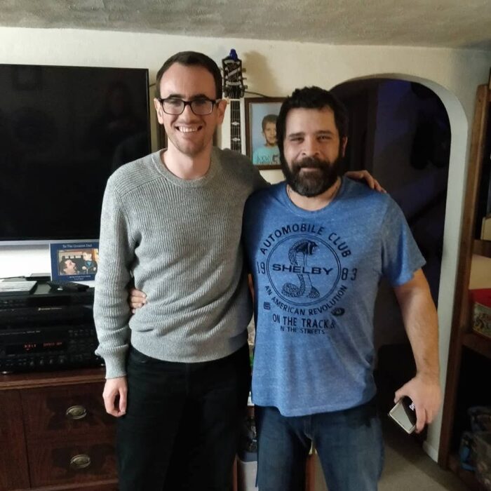 Two men standing close together, side by side, for a photograph. looking into the camera.
