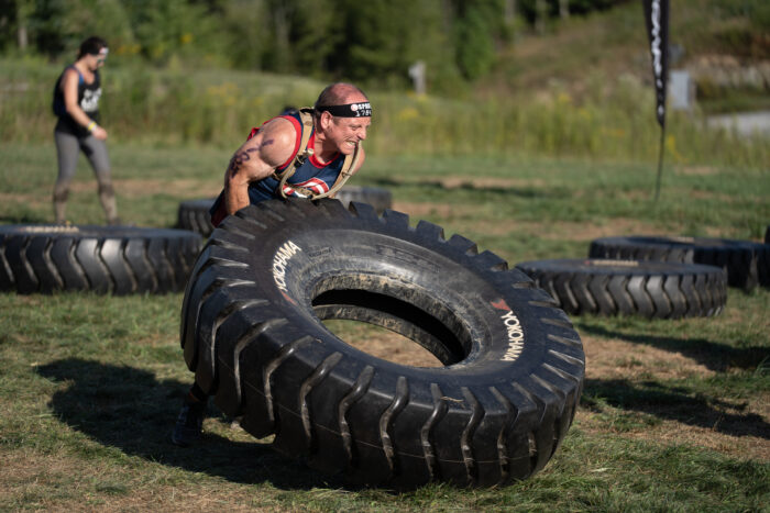 A man lifts a giant tire outside.
