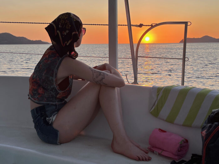 A young woman looks out toward the ocean from a boat at sunset.