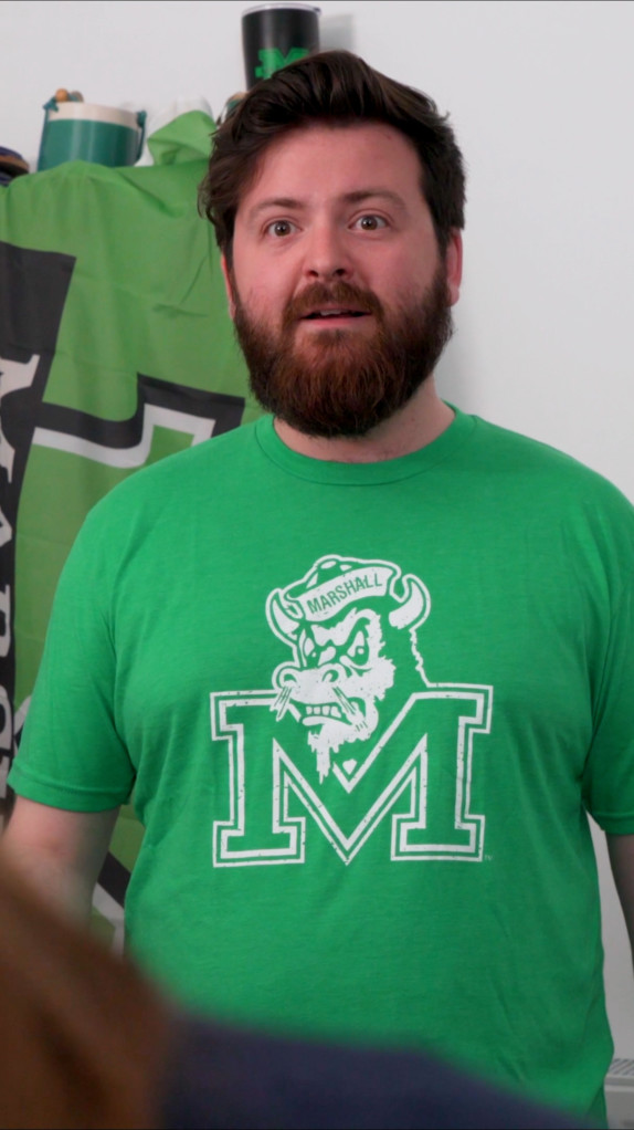 Man in green t-shirt and beard looks into the camera