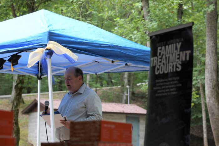 Man stands at a podium under a blue canopy