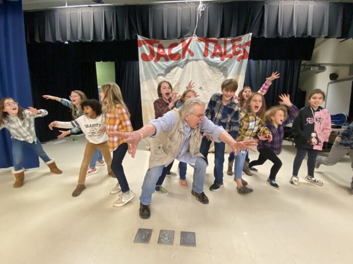 A man standing on a stage with a group of children. They are yelling and pointing. 