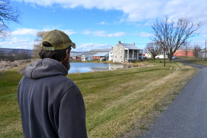 A man with his back turned to the camera. He is looking at a farm. 