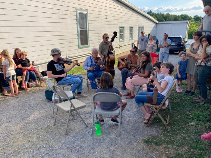 A group of people sitting and standing on a driveway playing music. 