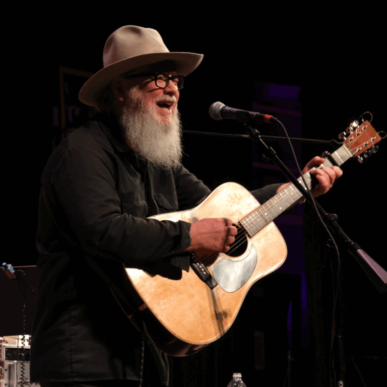 man in hat with beard plays guitar