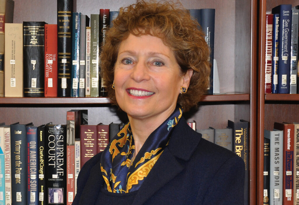 Woman in a dark jacket stands in front of a bookcase