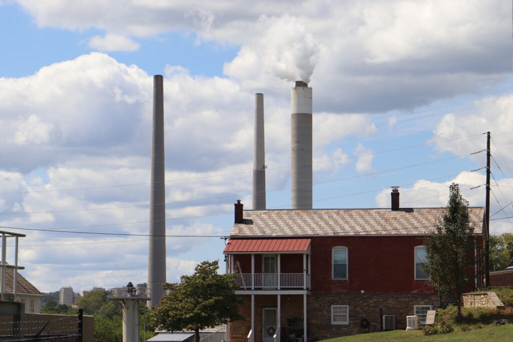 Smokestacks are seen in the distance against a cloudy, blue sky. A residential area is seen closer to the camera.