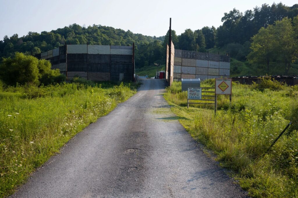 An unpaved road leads up to a fracking well pad, surrounded by bright green vegetation.