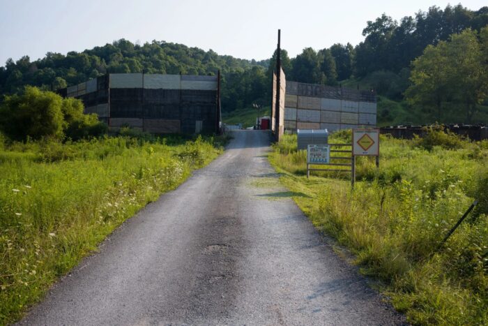 An unpaved road leads up to a fracking well pad, surrounded by bright green vegetation.