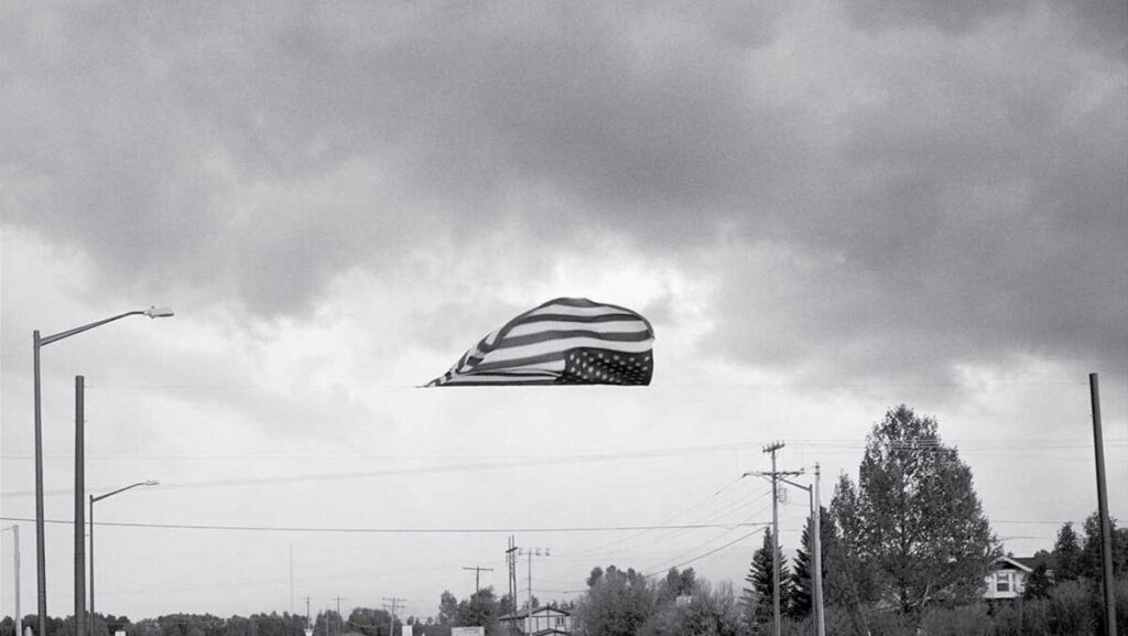 A black and white photo of an upside-down American flag hanging over an empty street.