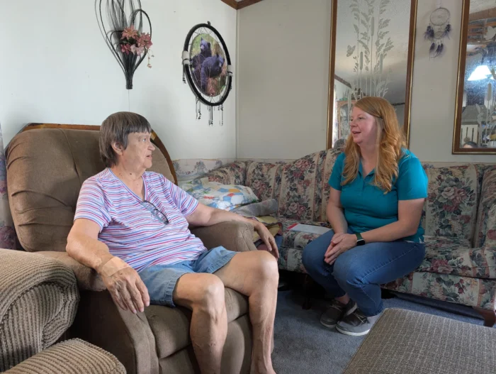Two white women sitting in a living room talking and facing one another.