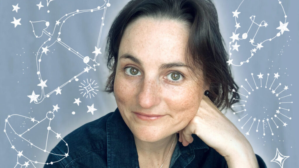 A white woman looking at a camera and posing with her hand on her face. She is wearing a navy-blue shirt and has short brown hair. There are illustrations of constellations around her on a blue background.