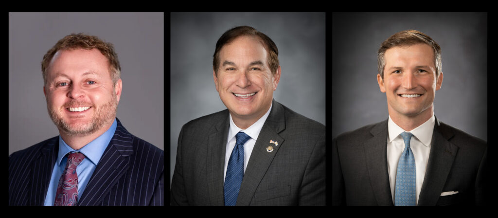 three men in suits look into the camera