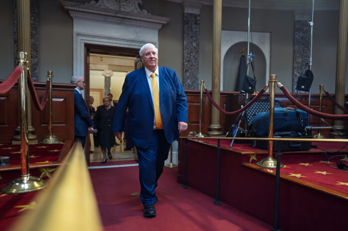 Large man in blue suit strides down a hallway