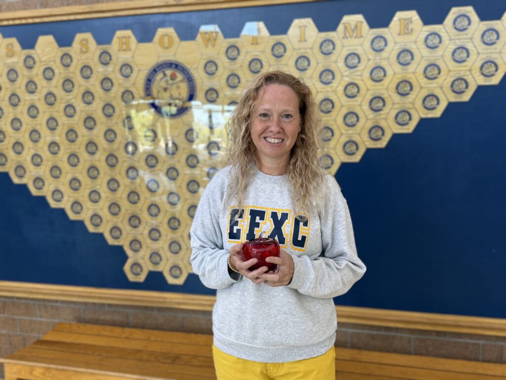 a white woman with long blonde wearing a sweater is holding a red glass apple.