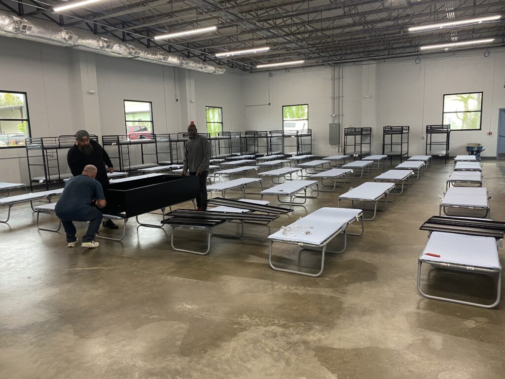 A large square room with rows of cots and bunk beds.