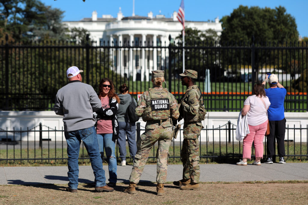 DC Federal Enforcement National Guard seen speaking to civilians in front of the White House on a sunny day.