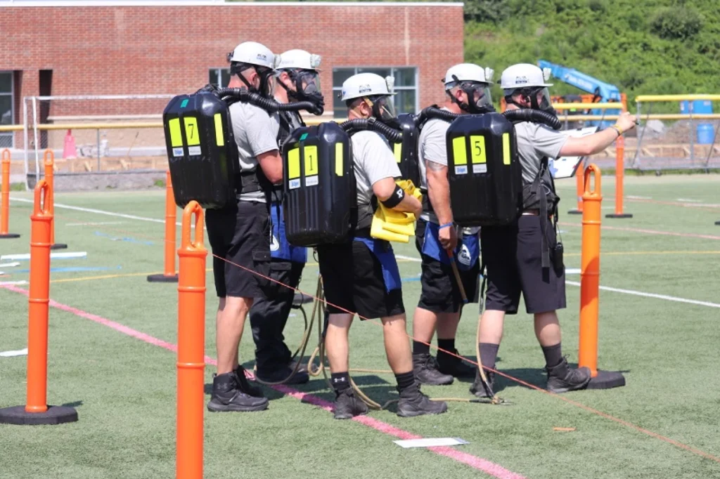 Five coal miners are shown on a sunny day dressed in rescue gear.