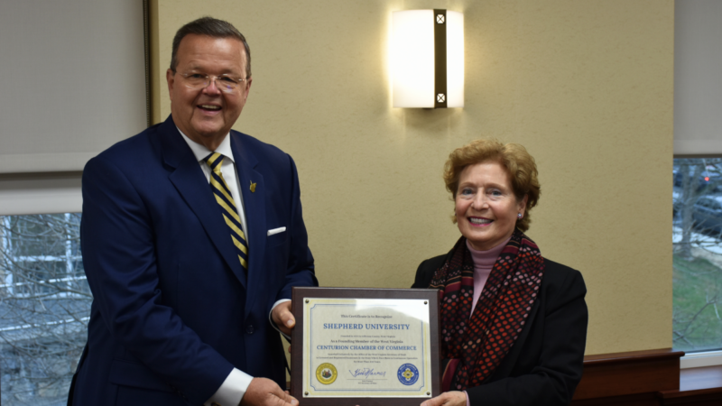 Two adults, a man and a woman, stand next to each other, smiling for the camera. They are dressed formally and are holding a certificate.