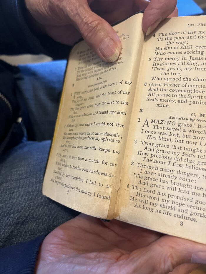 An aged book of music. An older woman is holding the pages. 