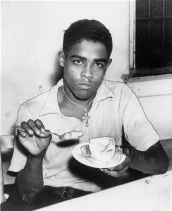 A black-and-white photo of a Black man eating from a plate.