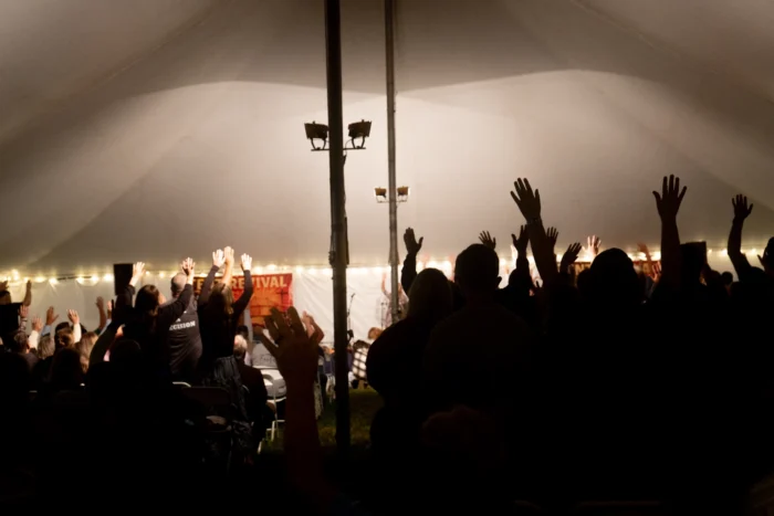 The silhouette of a group of people with their arms raised in a white tent. 