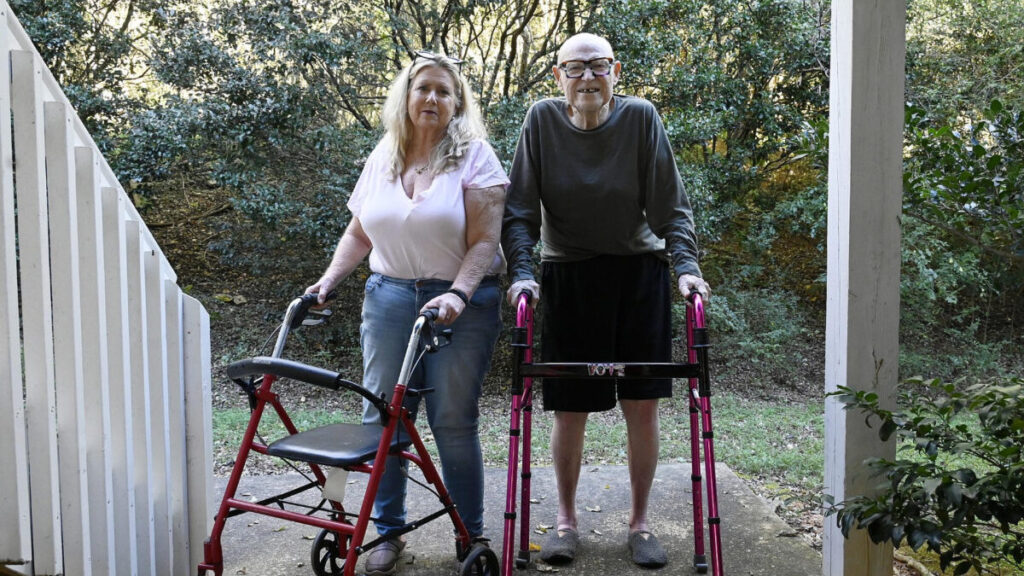 Two white people standing outside using walkers.