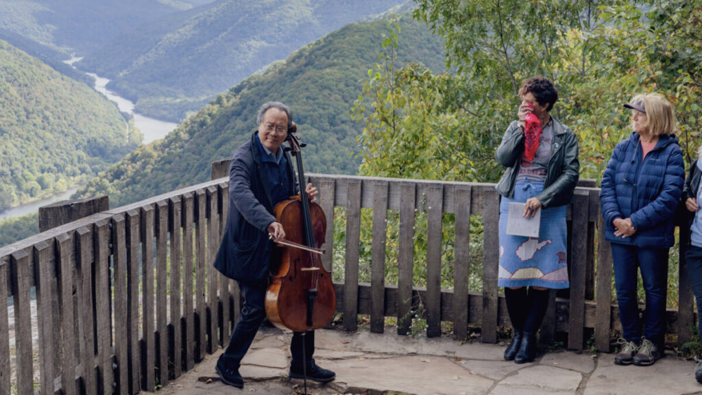 A man playing the cello on a lookout in front of a mountain gorge.