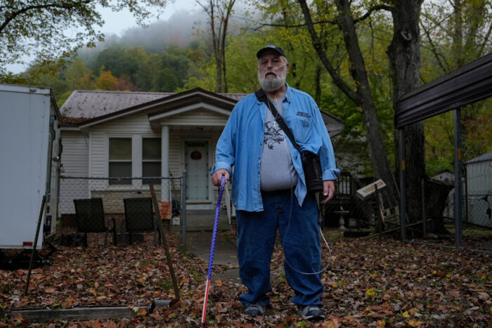 Man in blue stands in his front yard.