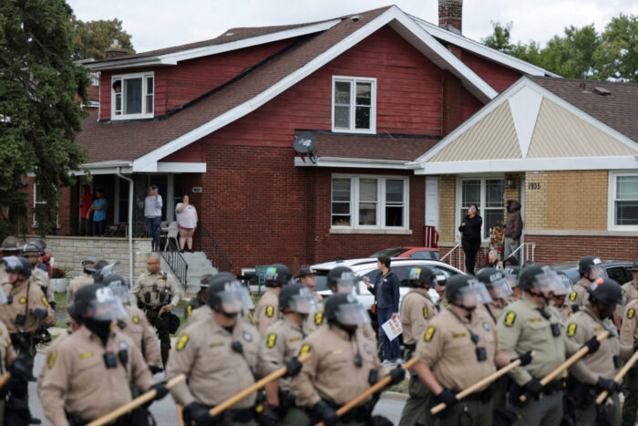 Dozens of ICE officers are seen standing in the streets of Chicago. They wear masks with shields and are seen next to residential homes.