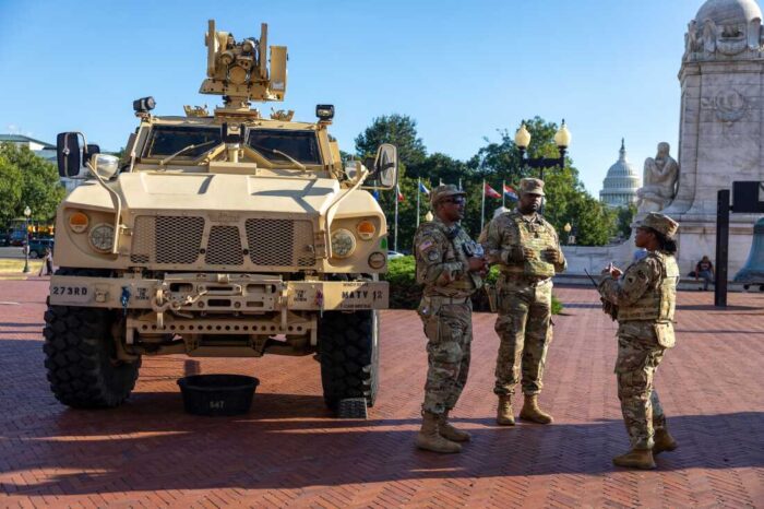 National Guard troops stand next to one of their armored vehicles on a sunny day.