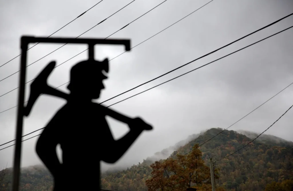 The silhouette of a coal miner statue looking on a foggy mountain.