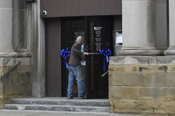 An older man walks into a building. There are blue ribbons on the front of the doors.