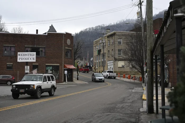 A small rural town on an overcast day. A car drives on the road toward the camera.