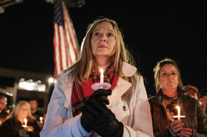 A woman stands at a candlelight vigil. She holds a candle and an American flag is seen behind her.