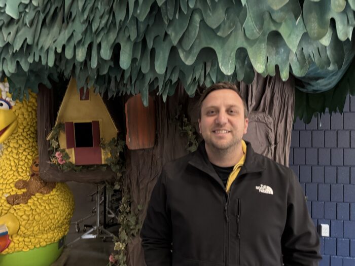 A man stands in front of a fake tree on a TV set.
