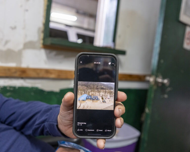 A hand holds a photo up toward the camera, showing a picture of a damaged garage shortly after a flood.