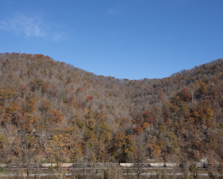 A faraway photo of coal cars moving along a train track.