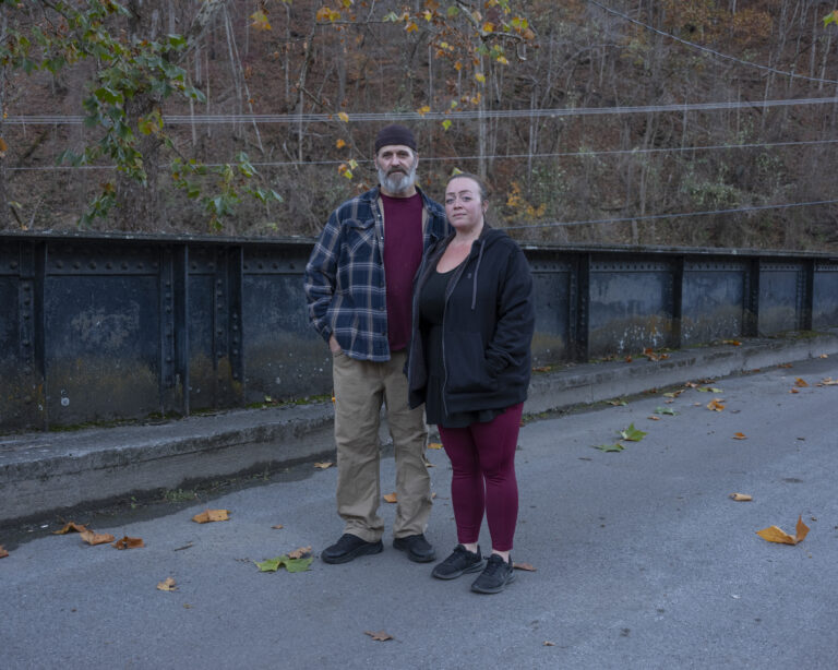 Two adults, a man and a woman, stand next to each other in front of a stone wall.
