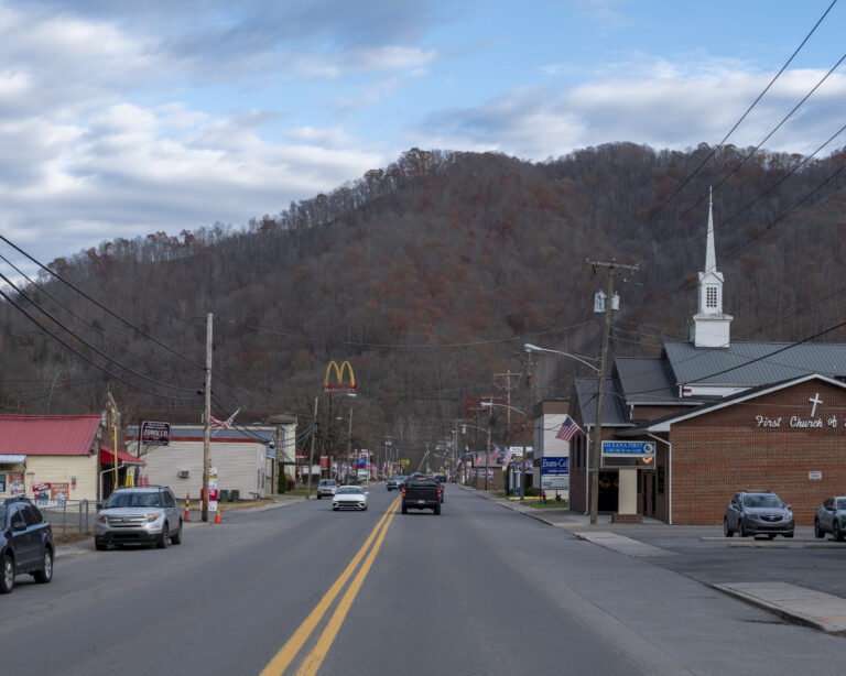 A faraway photo of a rural town. The persepective is from the middle of the road toward a hill.